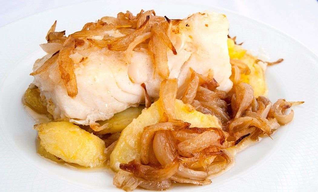 Ingredientes
4 lomos de bacalao
4 patatas grandes
3 cebollas grandes
1 vaso de Oporto blanco, coñac o brandy
1 cdita. pimentón dulce
Aceite de oliva virgen extra
Harina para rebozar
Sal (al gusto, recordad el punto de sal del bacalao)

Preparación

1. Pelamos la cebolla y la cortamos en juliana. Ponemos a calentar 5 cucharadas de aceite de oliva virgen extra en una sartén grande y añadimos la cebolla cuando este comience a estar caliente.
2. Rehogamos la cebolla hasta que esté bien blandita, unos 15 o 20 minutos. Retiramos la sartén del fuego y añadimos el pimentón dulce. 
3. Removemos para integrar con la cebolla y volvemos a poner la sartén al fuego. Añadimos el vino, dejamos que se reduzca durante dos minutos y retiramos. Reservamos para una fuente la cebolla y su salsa. La sartén la reutilizaremos posteriormente así que no la retiramos ya que aprovecharemos los jugos.
4. Pelamos las patatas y las cortamos en láminas finas, de 3 o 4 mm. de grosor. Calentamos abundante aceite en la sartén que hemos utilizado antes y freímos las patatas dejándolas un poquito crudas. Las patatas terminarán de cocinarse después en el horno. Reservamos.
5. Eliminamos el exceso de aceite y freímos los lomos de bacalao previamente enharinado. No es necesario que se frían demasiado, con darles un toque durante uno o dos minutos por cada lado es suficiente, así nos aseguramos que durante el horneado quede en su punto, jugoso y sabroso.
6. En una fuente apta para horno vamos montando el plato. Primero colocamos una base con las patatas, encima ponemos los lomos de bacalao y repartimos por encima y por los laterales la cebolla con toda su salsa.
7. Horneamos a 170º C con calor por arriba y por abajo, con el horno previamente caliente, durante 15 o 20 minutos.
8. Retiramos del horno y servimos caliente.
