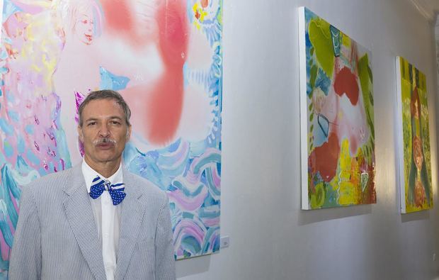 El pintor y arquitecto dominicano Alejandro Santana, junto a tres de los más de 200 cuadros y dibujos que integran su exposición.