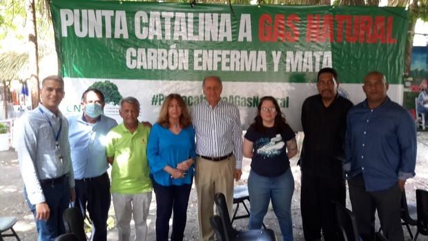 Participantes del Taller sobre el desarrollo de la provincia Peravia junto con los doctores José Serulle Ramia y Jacqueline Boin, posan teniendo de fondo el banner que reclama la conversión a gas natural de Punta Catalina.