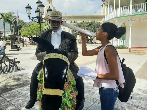 Una de las niñas lee sus poemas a un vendedor en burro, en el Parque Central de Puerto Plata.