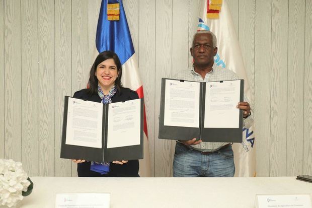 Biviana Riveiro Disla y Ernesto Peña Nina muestran el documento del acuerdo de firma acuerdo para promover la exportación e inversión en Constanza.