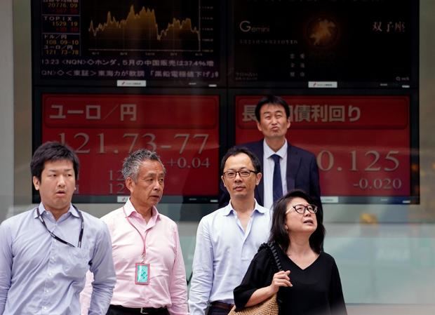 Varios peatones caminan junto a una pantalla que muestra información bursátil en Tokio, Japón.