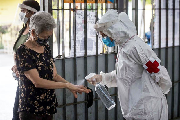 Personal sanitario rocía líquido desinfectante a una mujer.