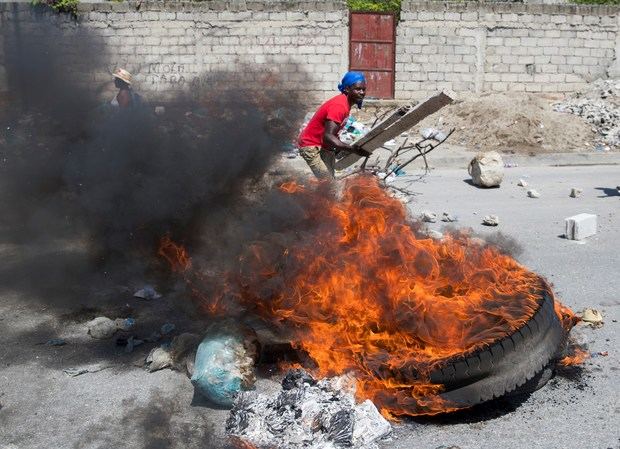 Un hombre aviva una barricada en llamas mientras cientos de seguidores del expresidente haitiano Jean Bertrand Aristide marchan exigiendo la dimisión del actual presidente, Jovenel Moise, este viernes, en Puerto Príncipe (Haití).