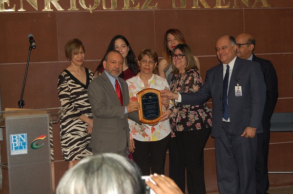 El director de la Biblioteca Nacional Pedro Henríquez Ureña, Dio medes Núñez Polanco, acompañado del escritor León Félix Batista, hace entrega de la placa de reconocimiento póstumo a la familia de la poeta Aida Cartagena Porta latín, integrada por Mayra Cartagena Salomón, Carlos Mesa Cartagena, Milagros Cartagena Infante, Cuqui Cartagena, Lesly Brea Cartagena y Miranda Brea.