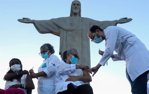 Dulcineia da Silva (i), 59, enfermera de la red pública de salud y Terezinha da Conceição (d), 80, que vive en un albergue para población en situación de vulnerabilidad social, son vacunadas hoy, lunes en un acto simbólico a los pies de la emblemática estatua del Cristo Redentor en el cerro del Corcovado, en Río de Janeiro.