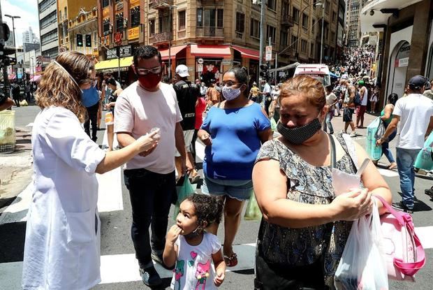 Una enfermera desinfecta las manos de las personas que caminan en una concurrida vía comercial en el centro de Sao Paulo, Brasil.