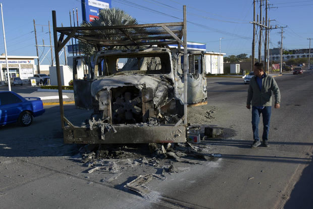 Una persona camina hoy a un costado de un vehículo calcinado tras los enfrentamientos de fuerzas federales con grupos armados ayer jueves, en la ciudad de Culiacán, estado de Sinaloa, México.