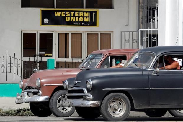 Dos autos clásicos pasan frente a una oficina de Western Unión, hoy en La Habana, Cuba. El cierre de todas las sucursales de Western Unión en Cuba como consecuencia de las últimas sanciones de Estados Unidos cercena una de las principales vías legales de envío de remesas a la isla, en medio de una grave crisis económica.