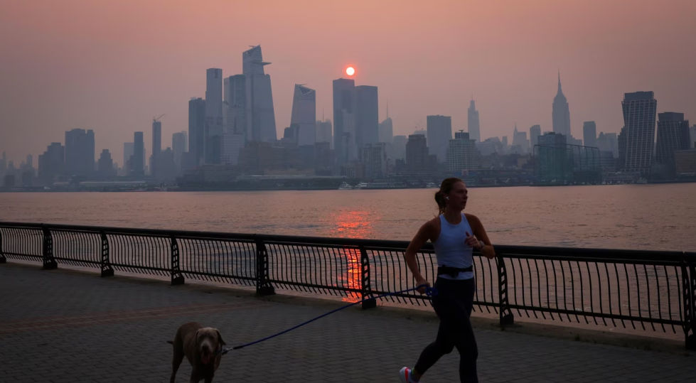 Una mujer trota con un perro a lo largo del río Hudson poco después del amanecer, mientras la neblina y el humo causados ​​por los incendios forestales en Canadá.