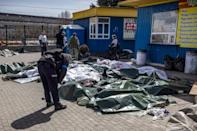 Un policía ucraniano se inclina ante unos cadáveres, cubiertos por lonas de plástico, tras el ataque con proyectiles a la estación de tren de Kramatorsk, el 8 de abril de 2022 al este de Ucrania.