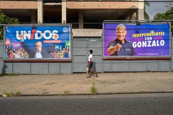 Hombres con tapabocas son vistos mientras pasan cerca a una valla publicitaria del candidato presidencial Luis Abinader, este sábado en Santo Domingo (República Dominicana). 
