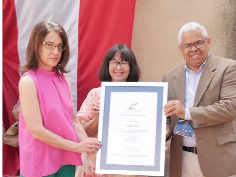 Momento en que la homenajeada Leibi Ng, recibe el pergamino de reconocimiento del de manos de la escritora Ruth Herrera, directora general del Libro y la Lectura y de la Feria del Libro, acompañada del escritor Valentín Amaro, miembro de la Comisión Organizadora de la Feria del Libro. (Foto:Cortesía).