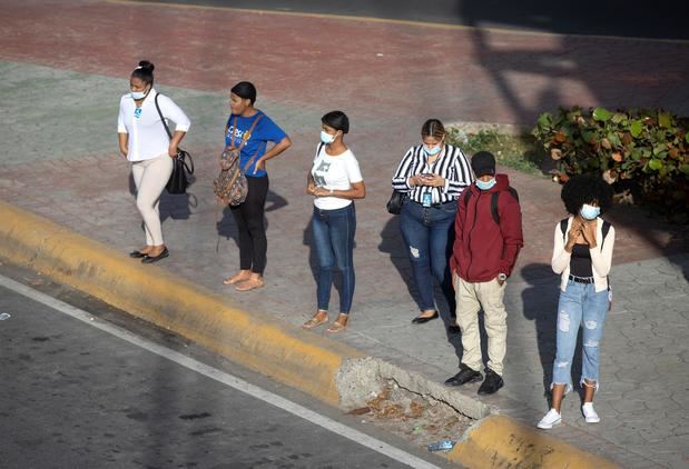 Personas esperan transporte público con la mascarilla puesta, hoy en Santo Domingo, República Dominicana.