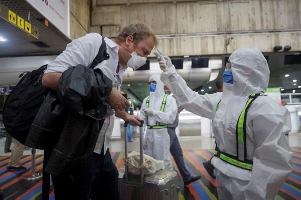 Un trabajador sanitario toma la temperatura de ciudadanos europeos que tomaron un vuelo hacia Madrid este jueves, en el Aeropuerto Internacional Simón Bolívar de Maiquetía, en La Guaira, Caracas (Venezuela).