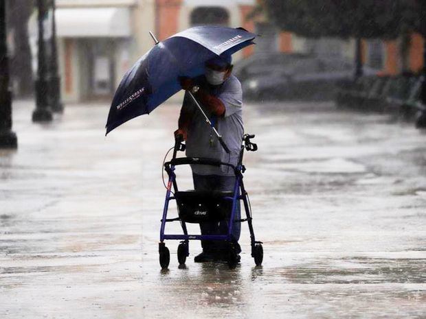 Un hombre que se apoya en un caminador lidia con su sombrilla durante la lluvia debido al paso de la tormenta Laura en Guayama, sur de Puerto Rico. 