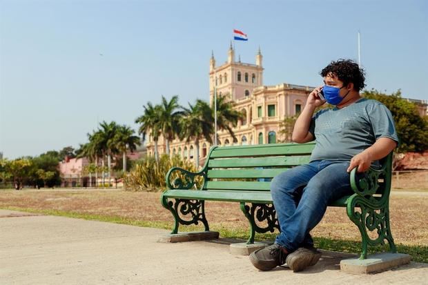 Un hombre protegido con tapabocas habla por celular en un asiento afuera del Palacio de Gobierno, también denominado Palacio de López en Asunción, Paraguay.
