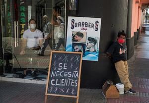 Un lustrabotas descansa este martes junto a un cartel con el mensaje “se necesita clientes”, colocado afuera de una barbería en la Zona Colonial, en Santo Domingo.
