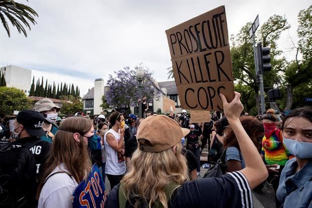 Un manifestante sostiene una pancarta que dice 'Enjuiciar a los policías asesinos' frente a la casa del alcalde de Los Ángeles Eric Garcetti mientras miles de manifestantes salieron a la calle para manifestarse tras la muerte de George Floyd, en Los Ángeles, California, EE. UU.