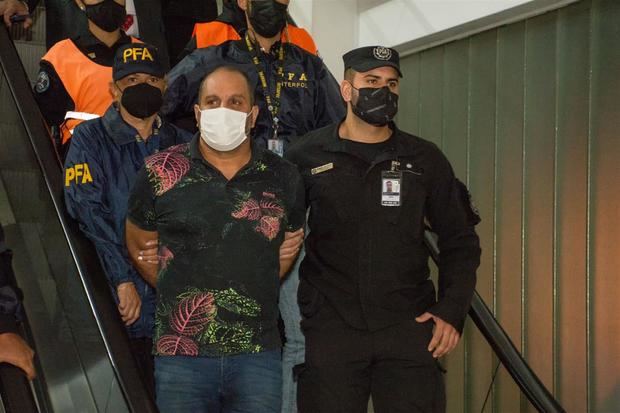 Fotografía cedida por la Policía de Seguridad Aeroportuaria (PSA) y la Policía Federal Argentina (PFA) que muestra al argentino Leonardo Cositorto (c) durante su arribó hoy al aeropuerto de Ezeiza, en Buenos Aires, Argentina.