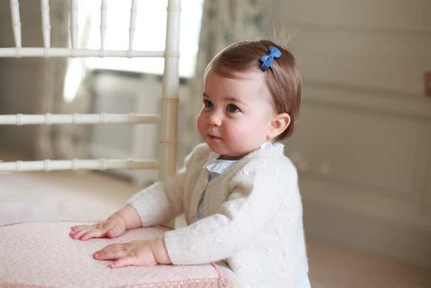 Carlota, peinada con el pelo sujeto con un lacito, aparece mirando hacia arriba, con grandes ojos azules y expresión seria, vestida con una blusa blanca y chaqueta de punto rosa.