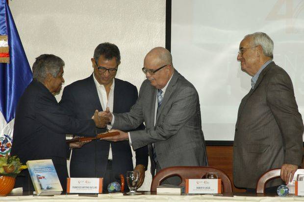 El profesor Francisco Antonio Avelino recibe la placa de reconocimiento a su trayectoria académica de Roberto Cassá. Observan Felix Jiménez y Antonio Guerra.