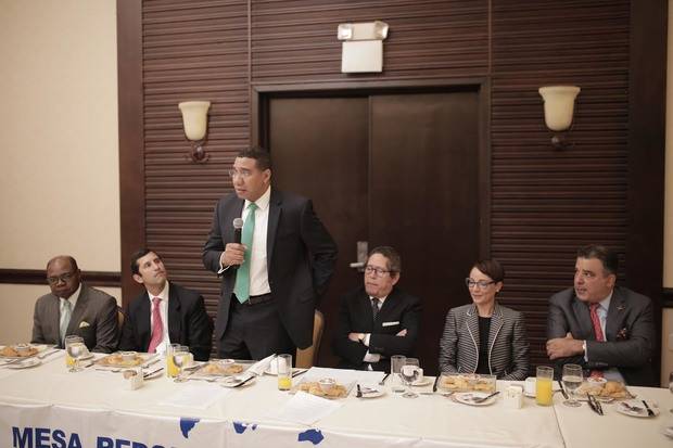 El primer Ministro de Jamaica, Andrew Holness, interviene en el encuentro, le acompañan en la mesa, Edmund Bartlett, ministro de Turismo de Jamaica; Roberto Herrera, presidente de la Asociación de la Industria Eléctrica; Fernando González Nicolás, presidente de la Mesa Redonda de la Mancomunidad en la República Dominicana; Kamina Johnson Smith, ministra de Relaciones Exteriores y Comercio Exterior de Jamaica, y Enrique De Marchena Kaluche, cónsul Honorario de Jamaica.