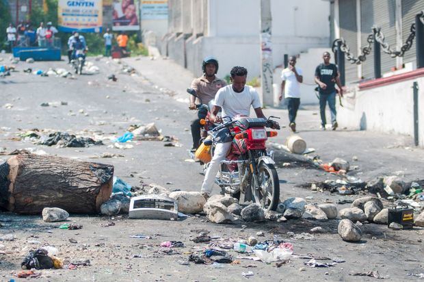 Personas en motocicleta pasan por una vía bloqueada con escombros durante una protesta este lunes, en Puerto Príncipe (Haití). Puerto Príncipe y otras ciudades de Haití se paralizaron en una nueva jornada de protestas por la escasez de combustible, que se prolonga desde el pasado agosto.