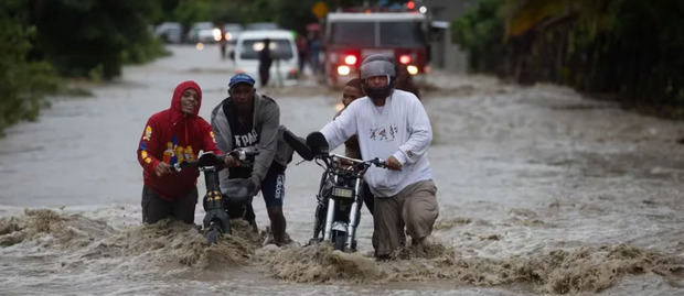 Personas cruzan con dificultad la carretera que se encuentra inundada producto de las intensas lluvias.