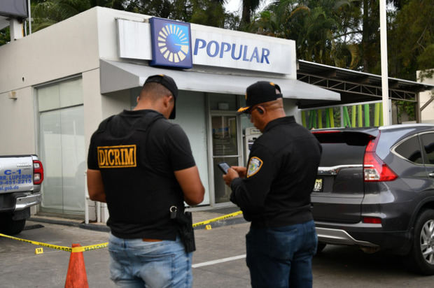 Agentes de la Dirección de Investigaciones Criminales de la Policía Nacional mientras hacían un levantamiento del asalto a la sucursal del Banco Popular.