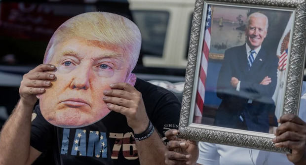 Un partidario de Joe Biden sostiene un retrato del presidente estadounidense (der) junto a un seguidor de Donald Trump que lleva una foto del exmandatario (izq) en Florida (EE.UU.).