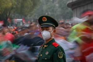 Corredores pasan detrás de un soldado chino ataviado con mascarilla durante el maratón de Pekín, China.