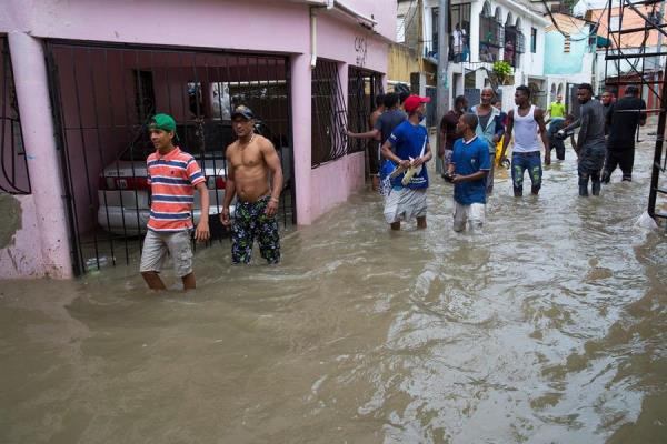 Personas caminan en una calle completamente inundada debido a las intensas lluvias de la tormenta Laura, este domingo en Santo Domingo (República Dominicana). 
