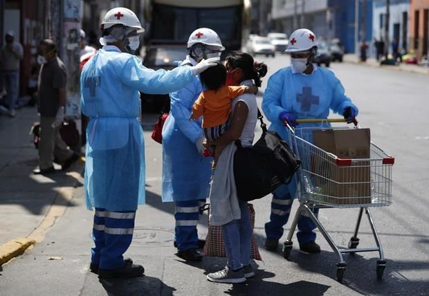 Personal de la Cruz Roja asisten a cientos de personas que esperan junto a una terminal de buses con la esperanza de poder regresar a sus lugares de origen en Lima, Perú. 