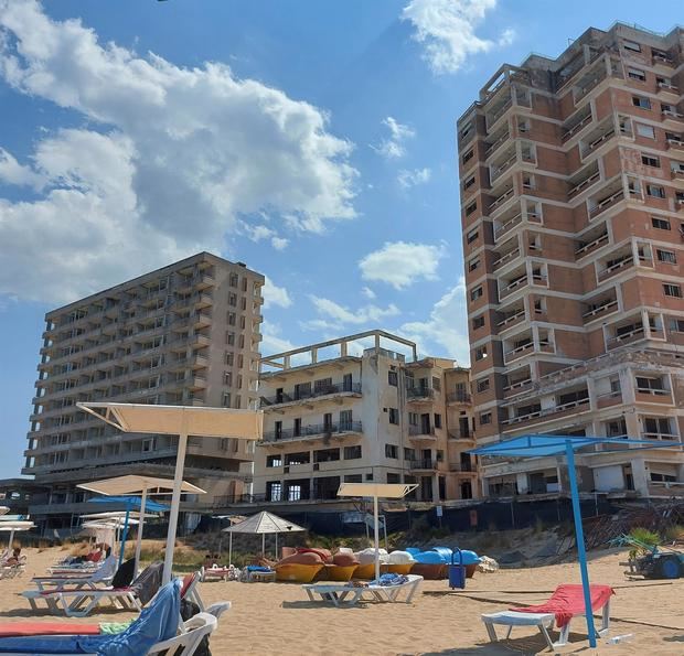 Algunos visitantes toman el sol en una playa preparada en el barrio de Varosha, sellado militarmente desde la invasión turca del norte de Chipre en 1974, bajo la sombra de los hoteles abandonados que aún a día de hoy muestran los signos de los bombardeos de los militares turcos.