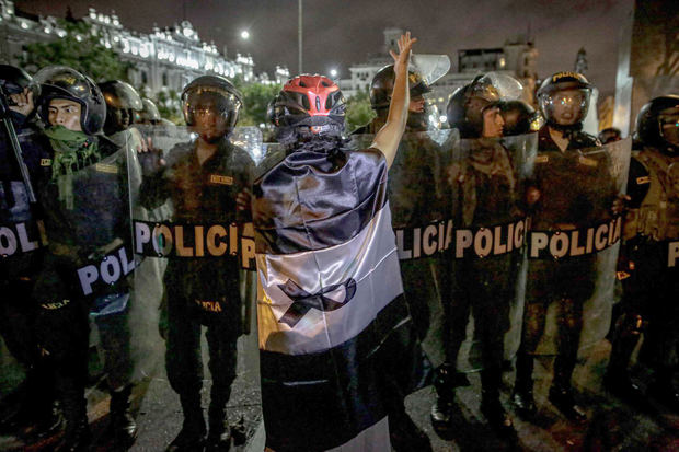 Un manifestante envuelto en una bandera peruana con color negro en lugar del rojo, se para frente a policías durante una movilización antigubernamental en el centro histórico de Lima (Perú), el 9 de febrero de 2023. 