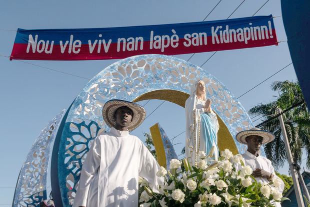 Fotografía de una imagen de la Virgen María durante su procesión, en el momento que pasa bajo un letrero en el que se lee en criollo haitiano 'Queremos vivir en paz sin secuestros!', durante la fiesta de la Inmaculada Concepción de la Virgen María, hoy, en Puerto Príncipe, Haití.