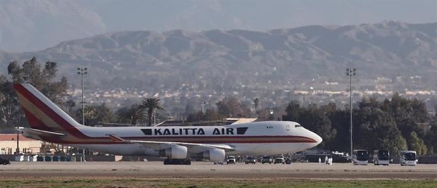 Las personas en trajes de materiales peligrosos se ven fuera del carguero Kalitta Air Boeing 747-400 mientras los autobuses se acercan al avión en la Base de la Reserva Aérea de Marzo que transporta a unos 200 evacuados estadounidenses en Riverside, California, EE. UU.