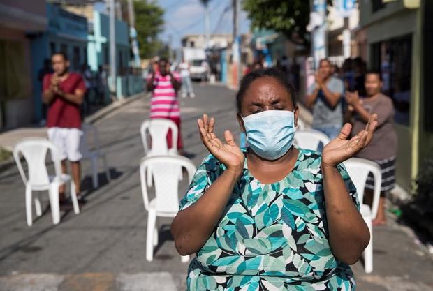 Decenas de personas cristianas, muchos usando mascarillas, se reúnen a orar momentos antes del inicio del toque de queda, este Viernes Santo en las calles del barrio María Auxiliadora, en Santo Domingo.