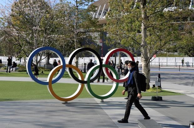 Un hombre con mascarilla pasa junto a los aros olímpicos situados frente al Estadio Olímpico de Tokio, Japón.