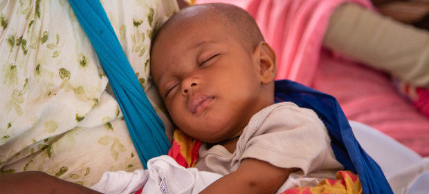 Un bebé duerme en los brazos de su madre en espera de recibir una vacuna.