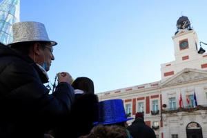 Unas personas se comen las uvas aprovechando las campanadas de las doce del mediodía en la Puerta del Sol este jueves, último día del año que nos dejará unas campanadas insólitas ya que la Puerta del Sol estará vacía debido a las restricciones por el coronavirus. EFE/Fernando Alvarado