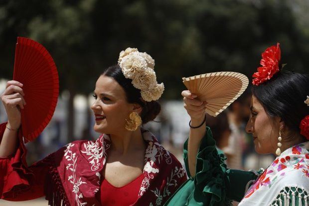 Varias mujeres vestidas de flamenca se cubren los ojos con abanicos en el recinto ferial del Arenal durante la Feria de Nuestra Señora de la Salud en Córdoba. EFE/Salas