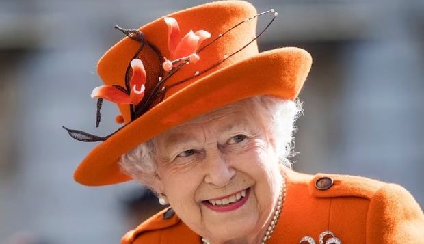 Look en naranja intenso, con sombrero decorado con flores y ramas marrones, equilibrado por perlas y broche en espiral con cristales.