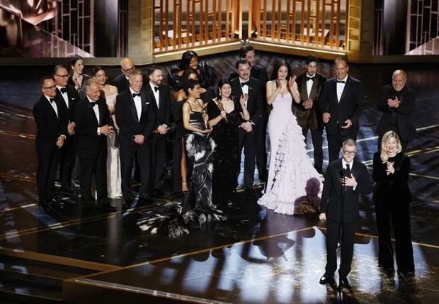 El director Paul Thomas Anderson (i) y la productora Sara Murphy (d) hablan frente al elenco de ‘One Battle After Another’ al recibir el Óscar a mejor película en la edición 98.ª de los premios de la Academia.