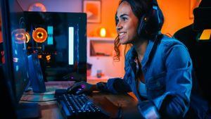 Bonita y emocionada chica Gamer negra con auriculares está jugando un videojuego en línea de disparos en primera persona en su computadora. La habitación y la PC tienen luces LED de neón de colores. Noche acogedora en casa.